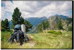 A backpack sits on a grassy hillside with mountains in the background